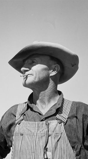 grayscale photography of man in overalls and cap thumbnail