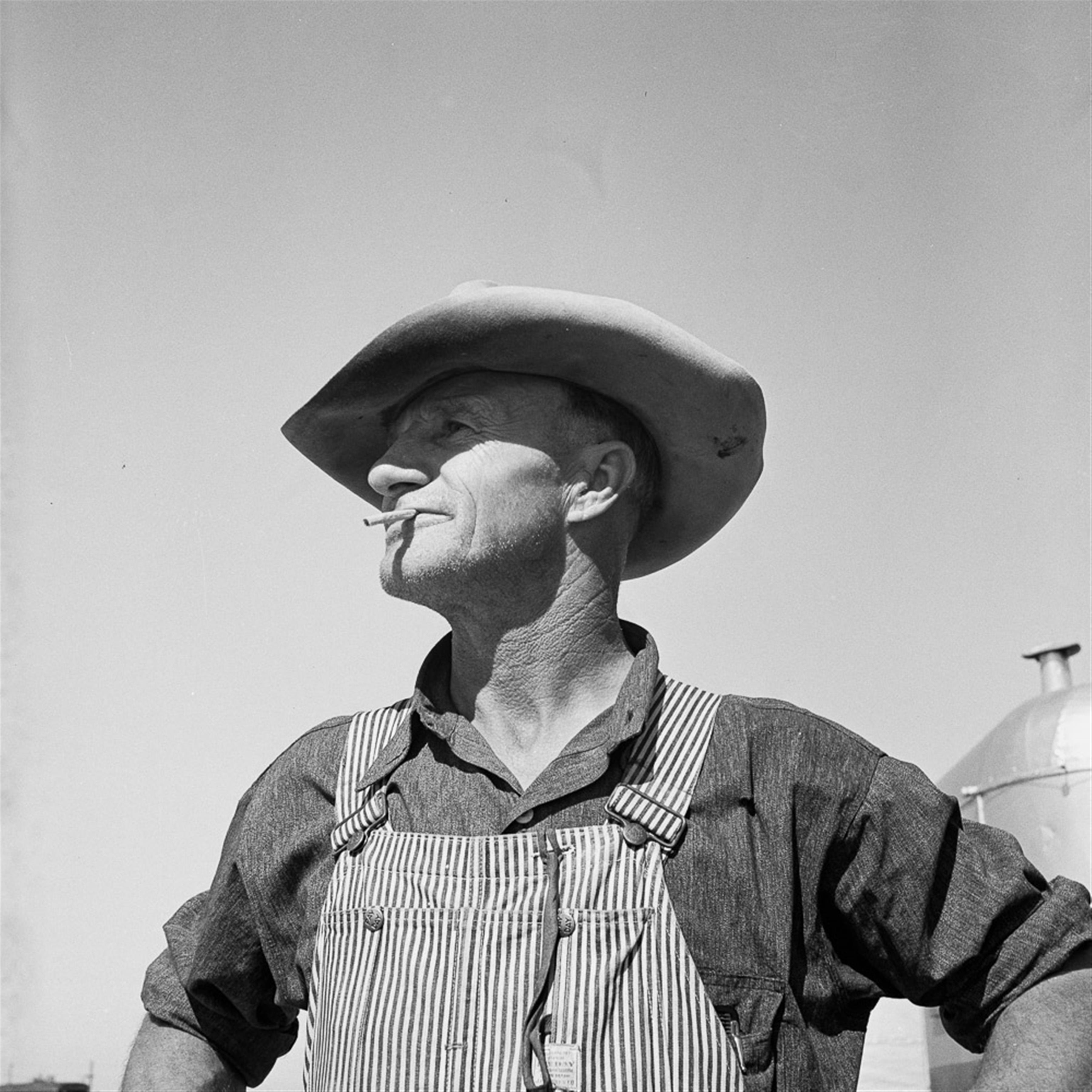 grayscale photography of man in overalls and cap