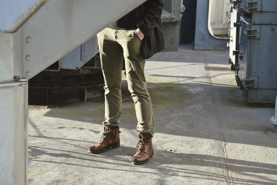 person wearing green pants and brown leather work boots standing near gray  metal electric panels free image