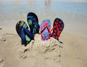 two pair of flip flops on the sand near water at daytime thumbnail