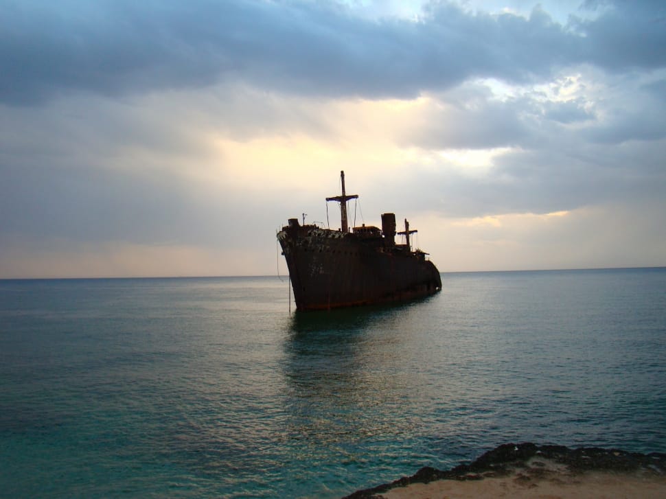 rusted gray ship on body of water under cloudy skyy preview