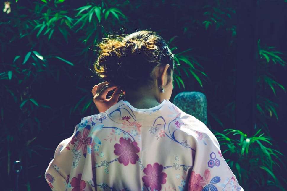 woman in floral dress touching her tied hair near garden preview