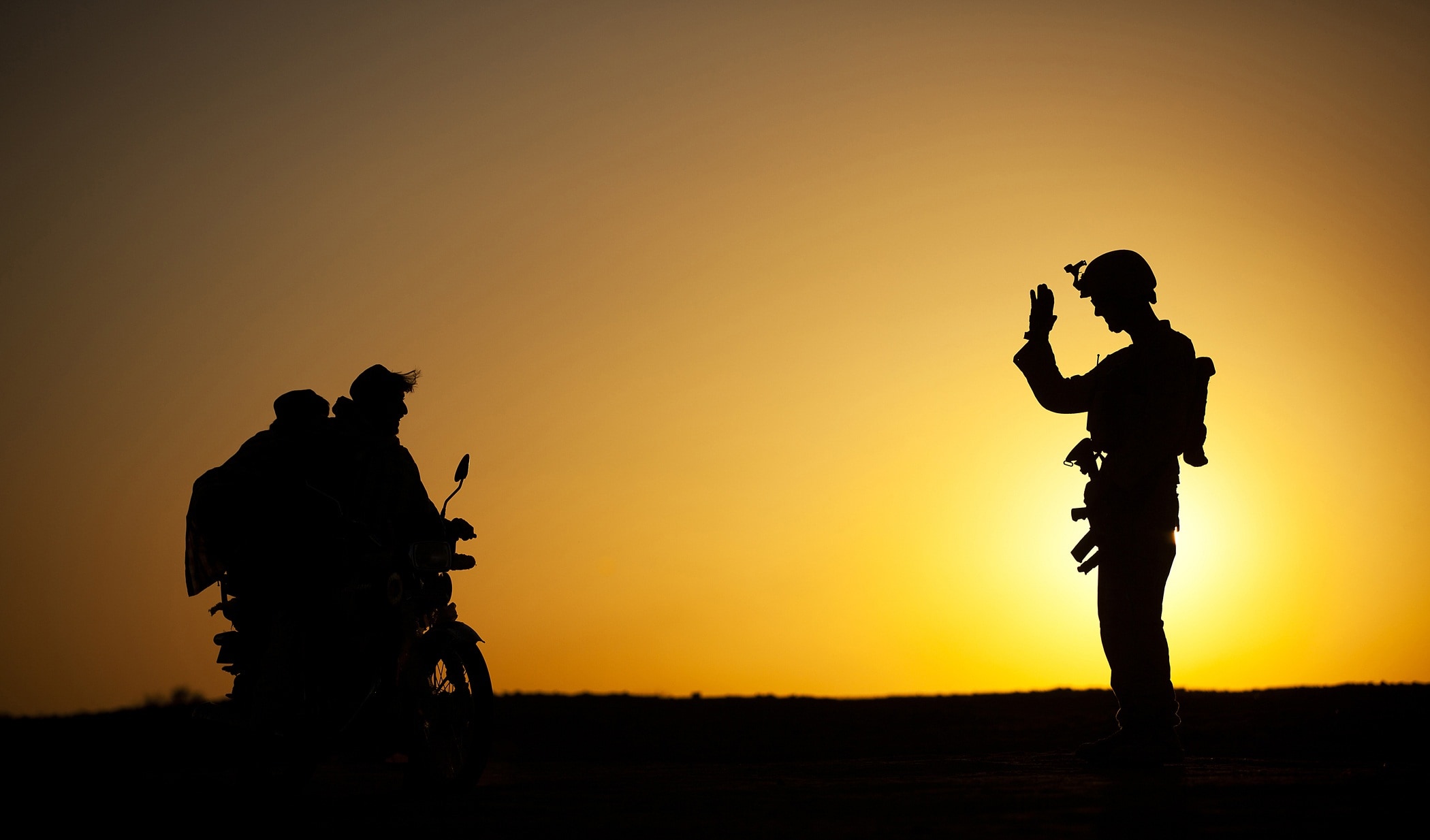 silhouette photo of soldier waving hand in front of two people riding motorcycle