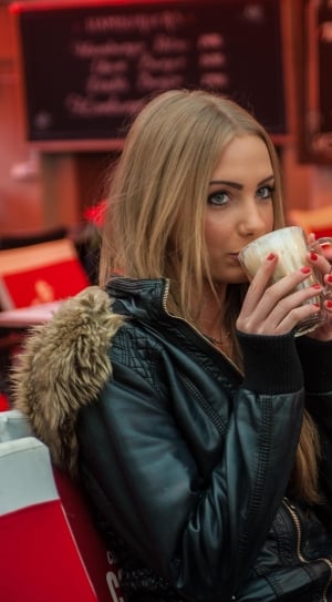 woman in black parka jacket sitting on a chair while holding a mug thumbnail