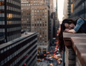 Brown Haired Woman Leaning on Edge of Buidling in City thumbnail