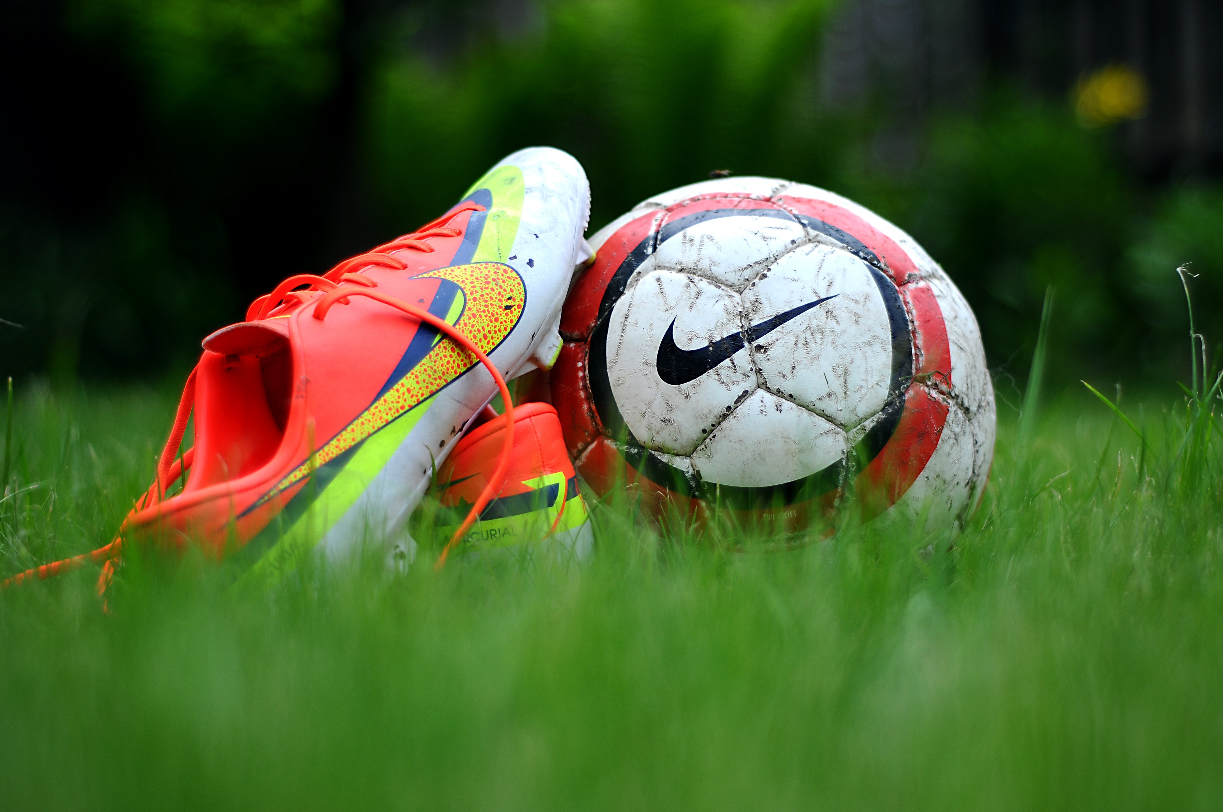 close up photography of Nike soccer cleats and soccer ball on green grass field during daytime