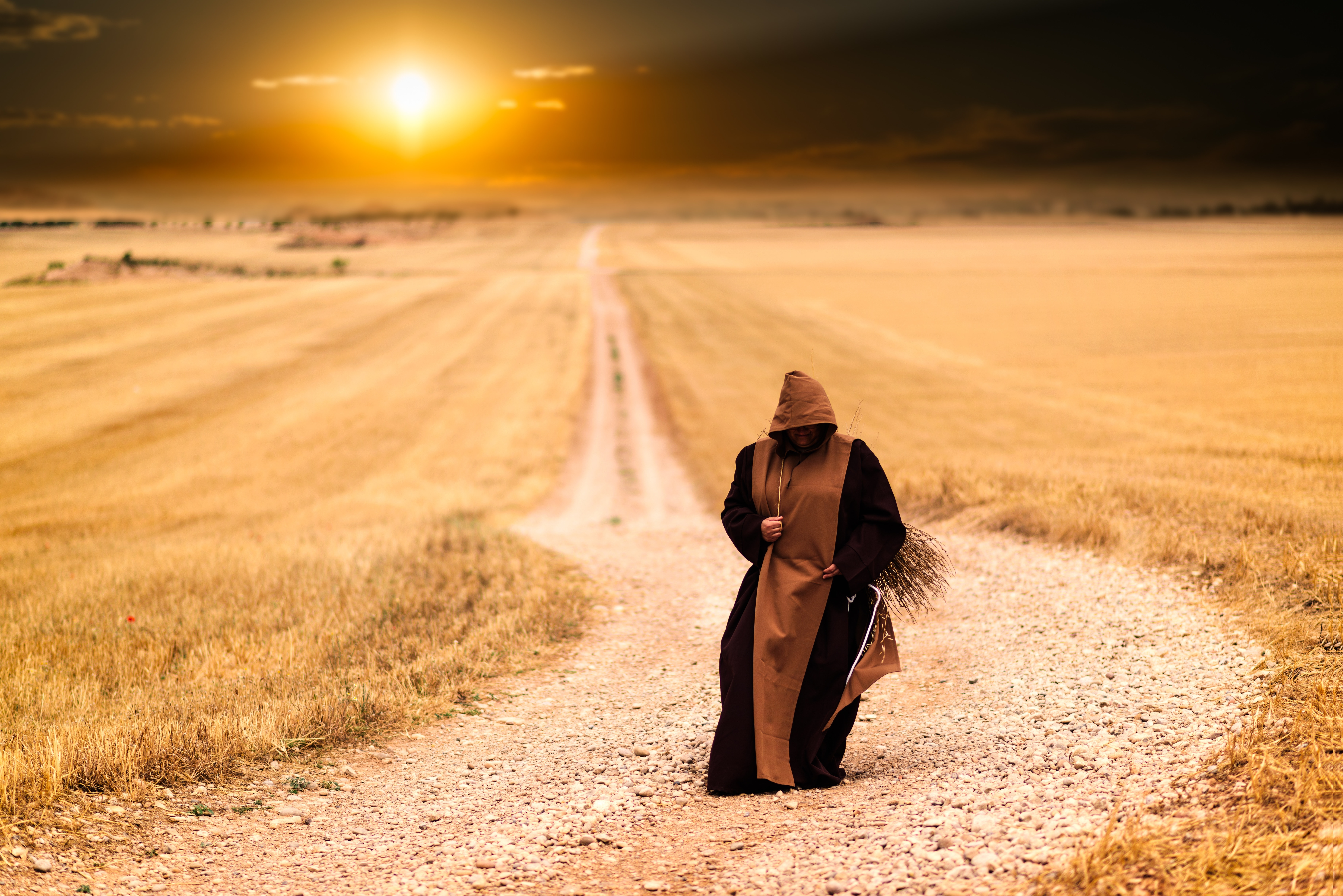 person in brown hooded dress walking on brown field photo
