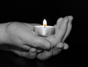 gray scale photo of hand holding tealight candle thumbnail