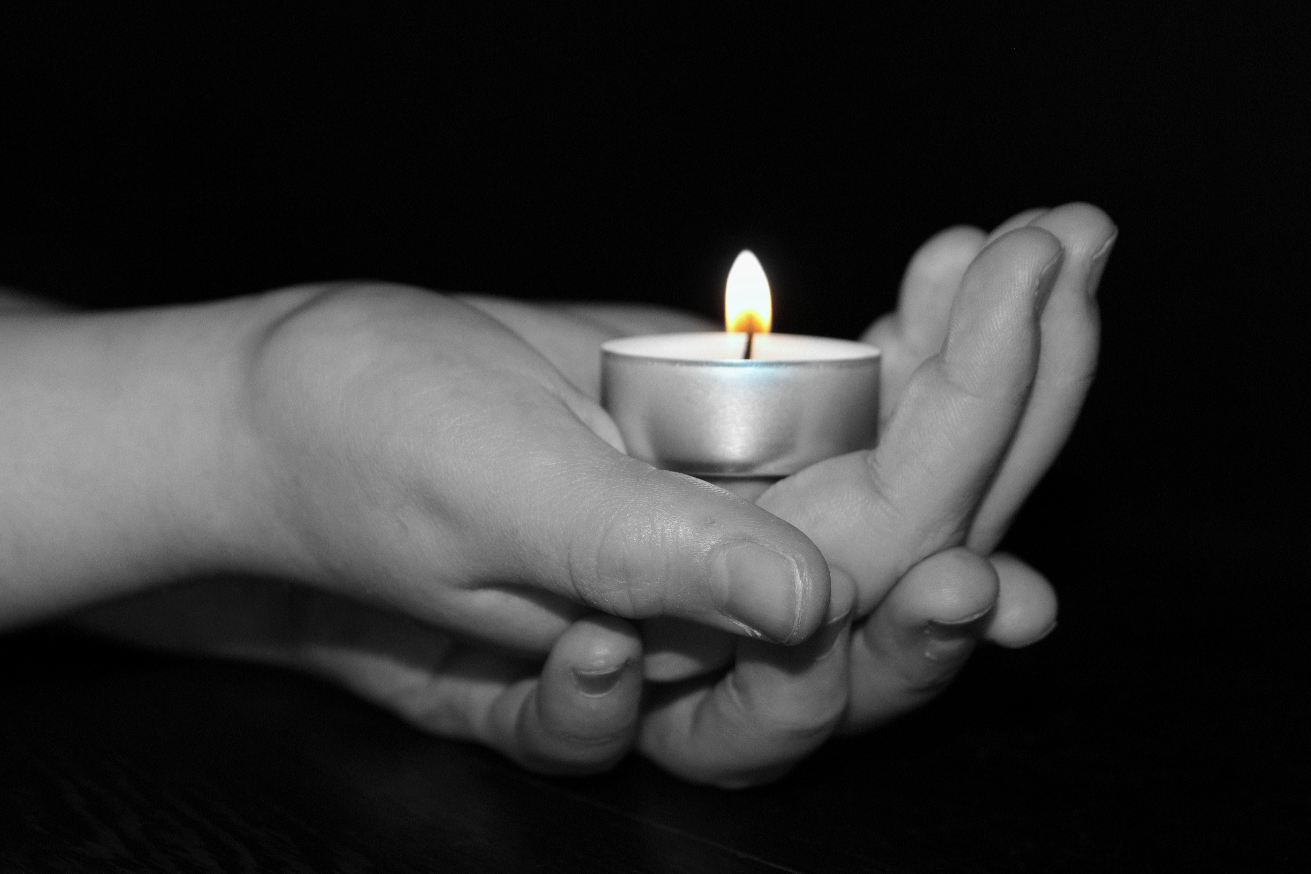 gray scale photo of hand holding tealight candle