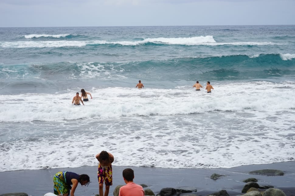 5 persons swimming at beach near 3 persons at gray seashore during daytime preview