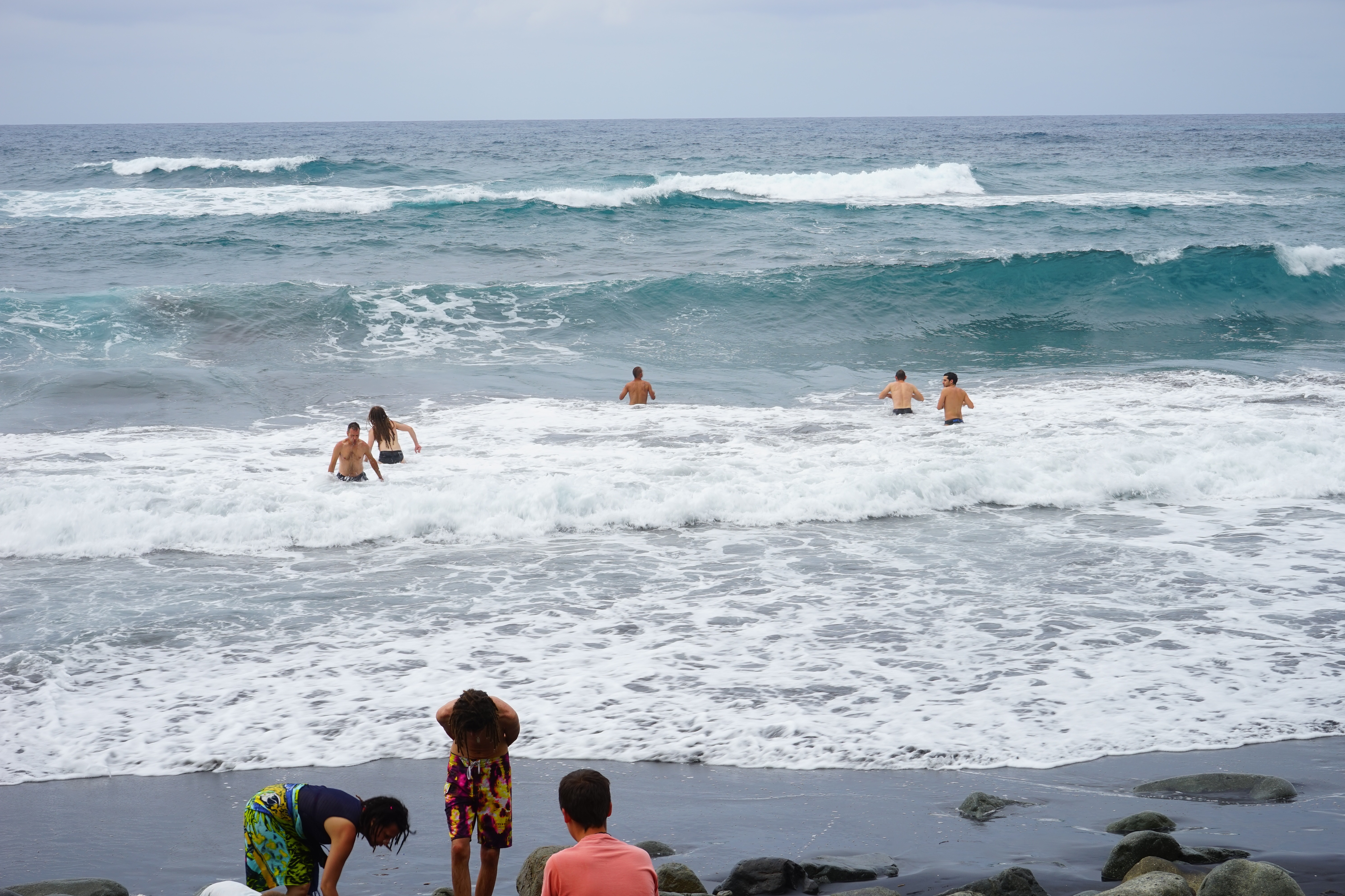 5 persons swimming at beach near 3 persons at gray seashore during daytime