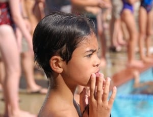 close up photo of boy holding hes mouth with both hands while standing nearby crowded swimming pool thumbnail