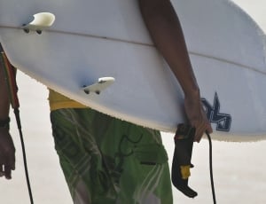 person wearing green boardshort carrying surfboard thumbnail