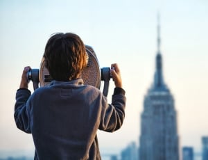 boy using telescope to see empire state building during day time thumbnail