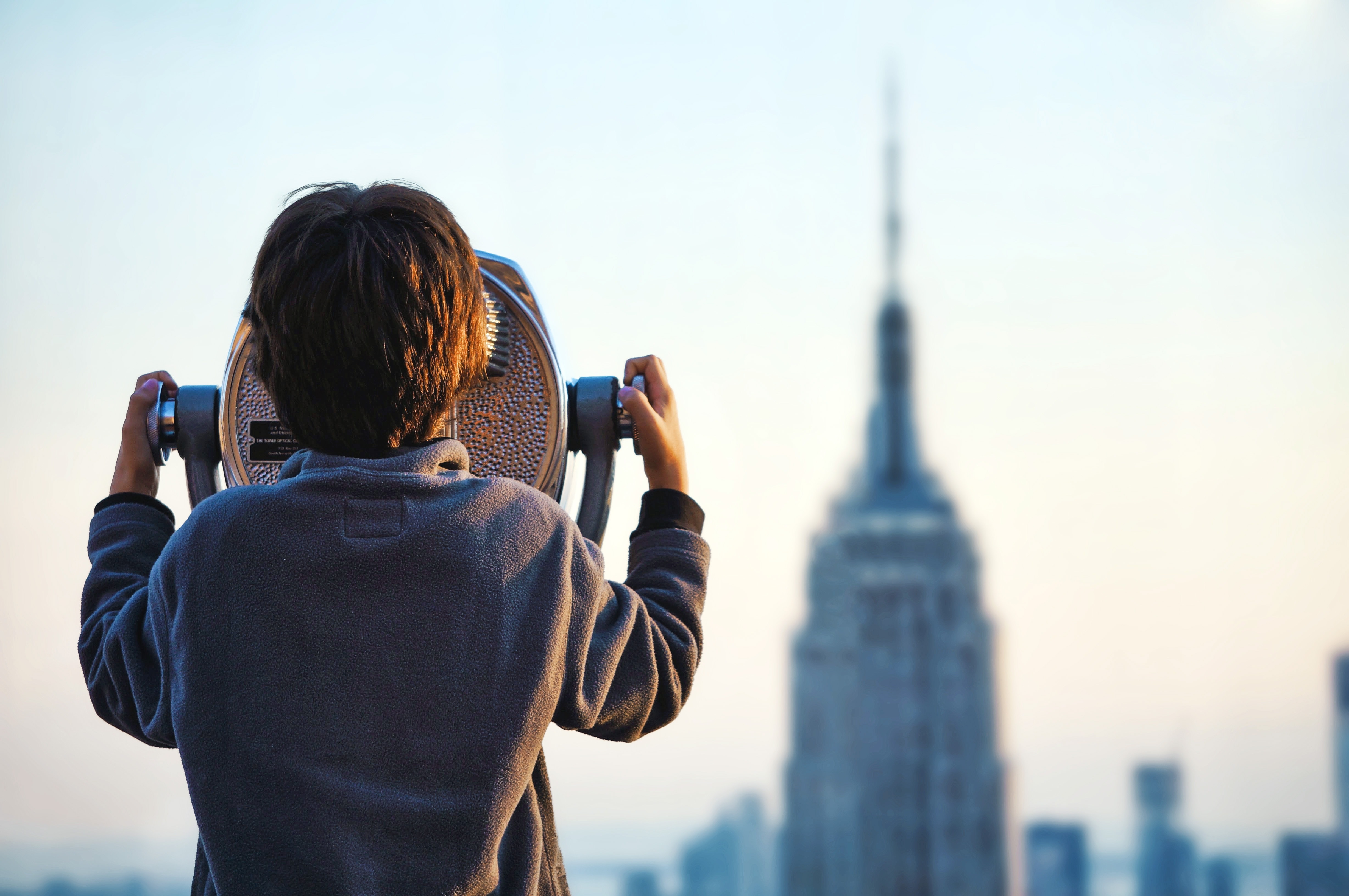 boy using telescope to see empire state building during day time