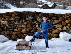 boy wearing black and blue striped long sleeve shirt standing on snow thumbnail