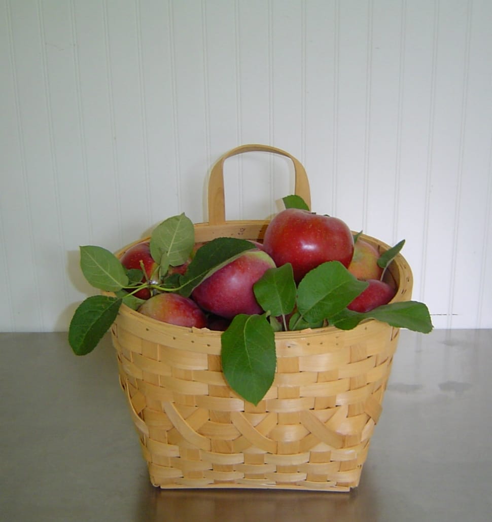 ripe apples with leaves in brown wicker basket on grey surface preview