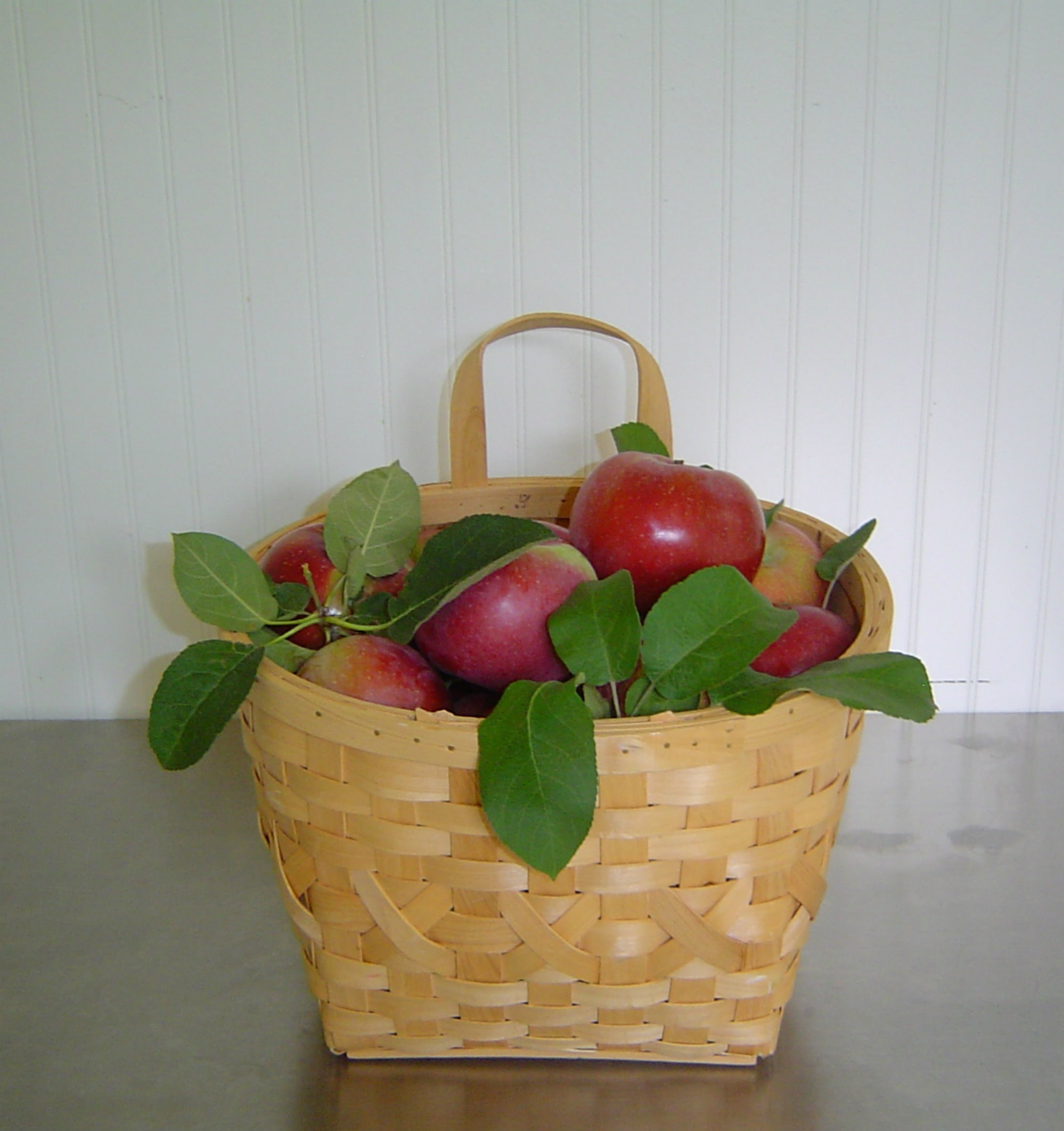ripe apples with leaves in brown wicker basket on grey surface