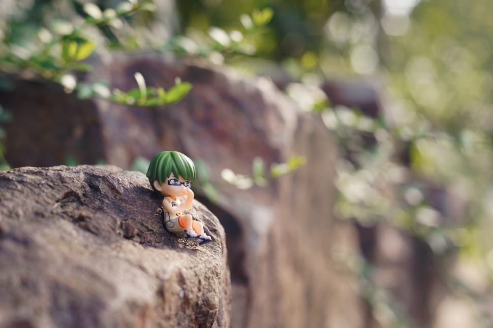 male anime character with green hair figurine on brown rock photo during daytime preview