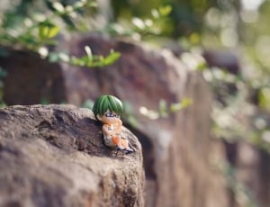 male anime character with green hair figurine on brown rock photo during daytime thumbnail