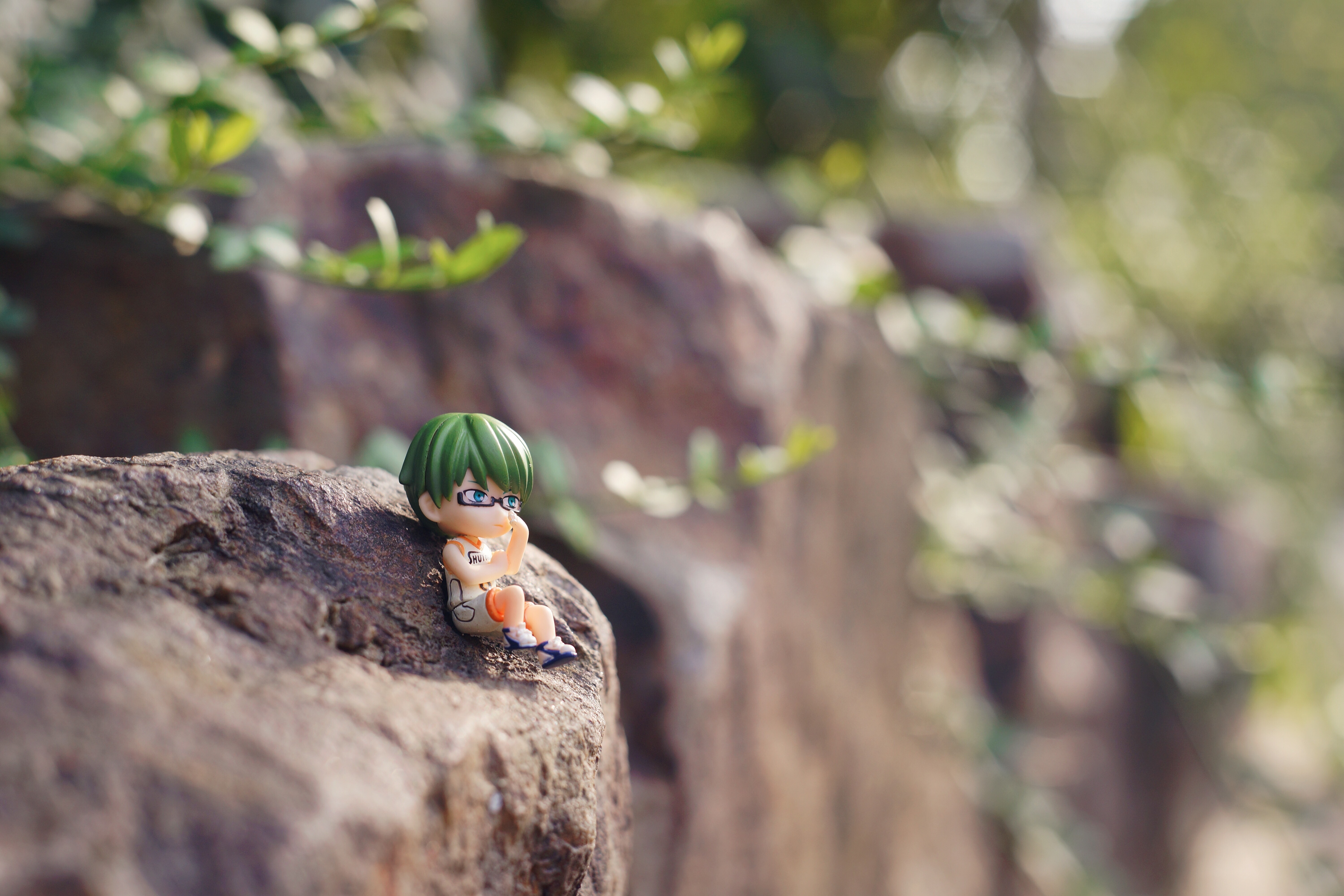 male anime character with green hair figurine on brown rock photo during daytime