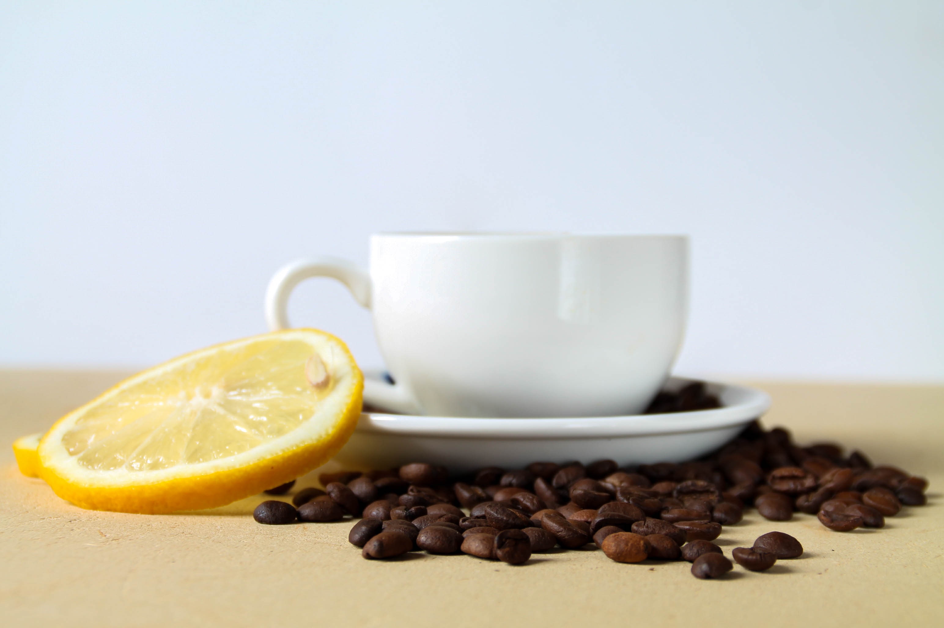 white ceramic cup on saucer surrounded by coffee beans beside slice of lemon