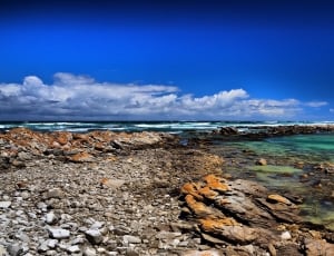 rocky sea shore under blue and cloudy sky thumbnail