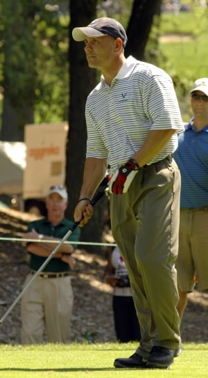 man in gray polo shirt and green dress pants playing golf thumbnail