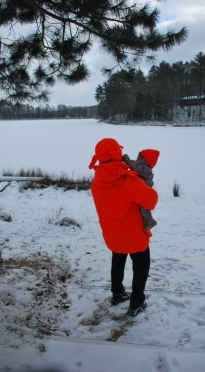person carrying baby standing on the snowy field thumbnail