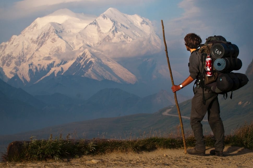 man holding stick while carrying hiking backpack preview