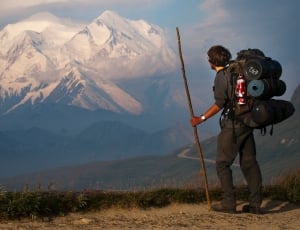 man holding stick while carrying hiking backpack thumbnail