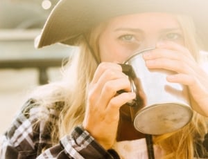 selective focus photography of woman in brown and white plaid long sleeve shirt drinking on stainless steel cup thumbnail