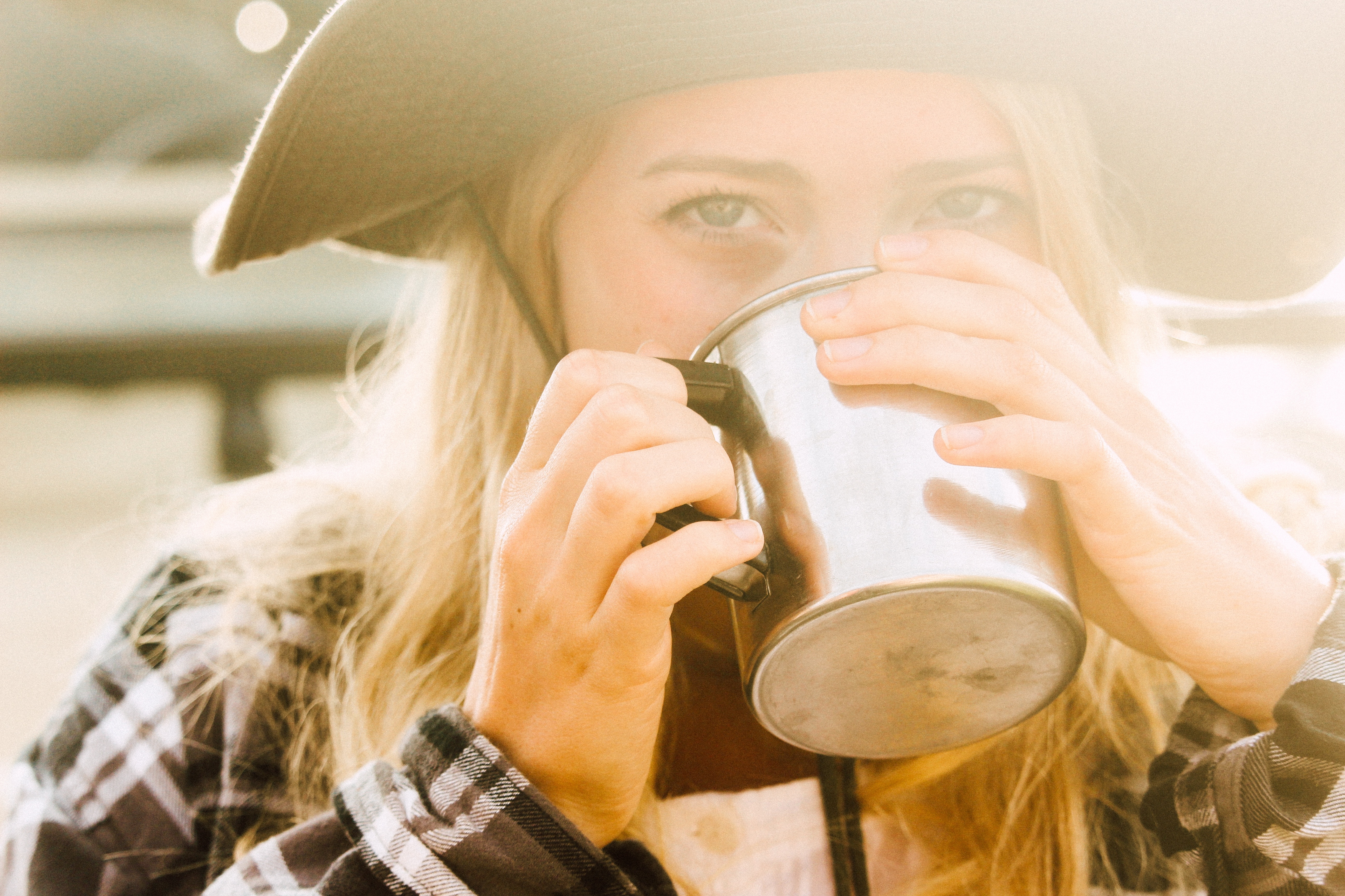 selective focus photography of woman in brown and white plaid long sleeve shirt drinking on stainless steel cup