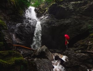 person holding red umbrella standing watching waterfalls during daytime thumbnail