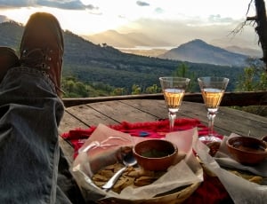 person's feet on table beside dish and champagne glasses during daytime thumbnail