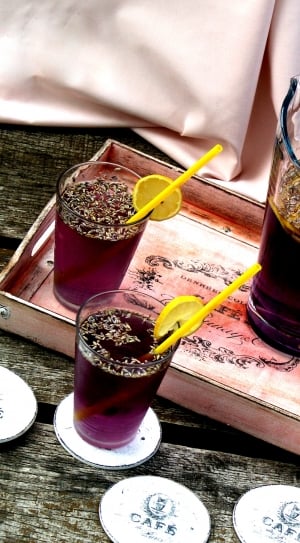 grape juice with slices of lemons and straws near wooden tray with glass pitcher filled with grape juice thumbnail