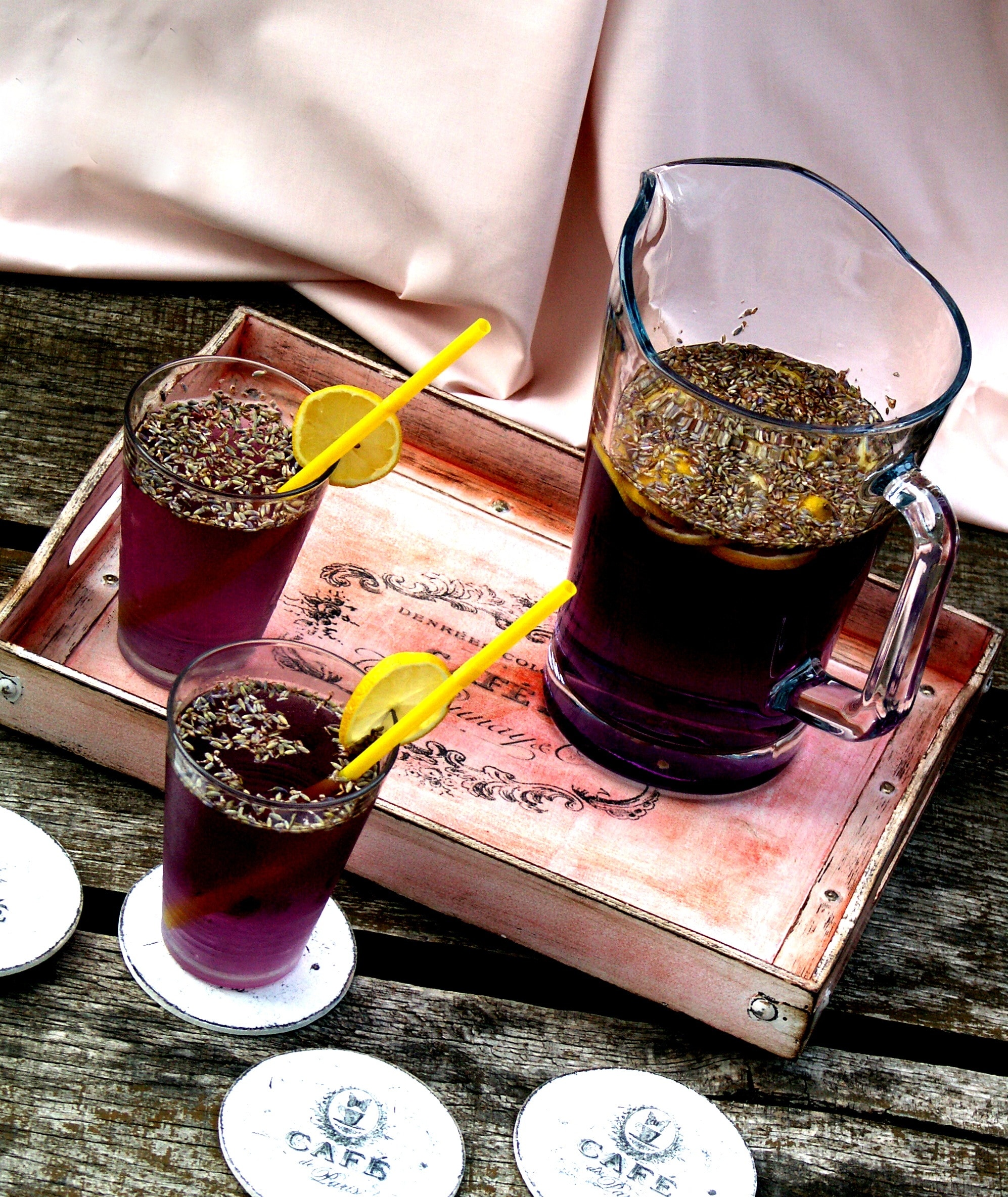 grape juice with slices of lemons and straws near wooden tray with glass pitcher filled with grape juice