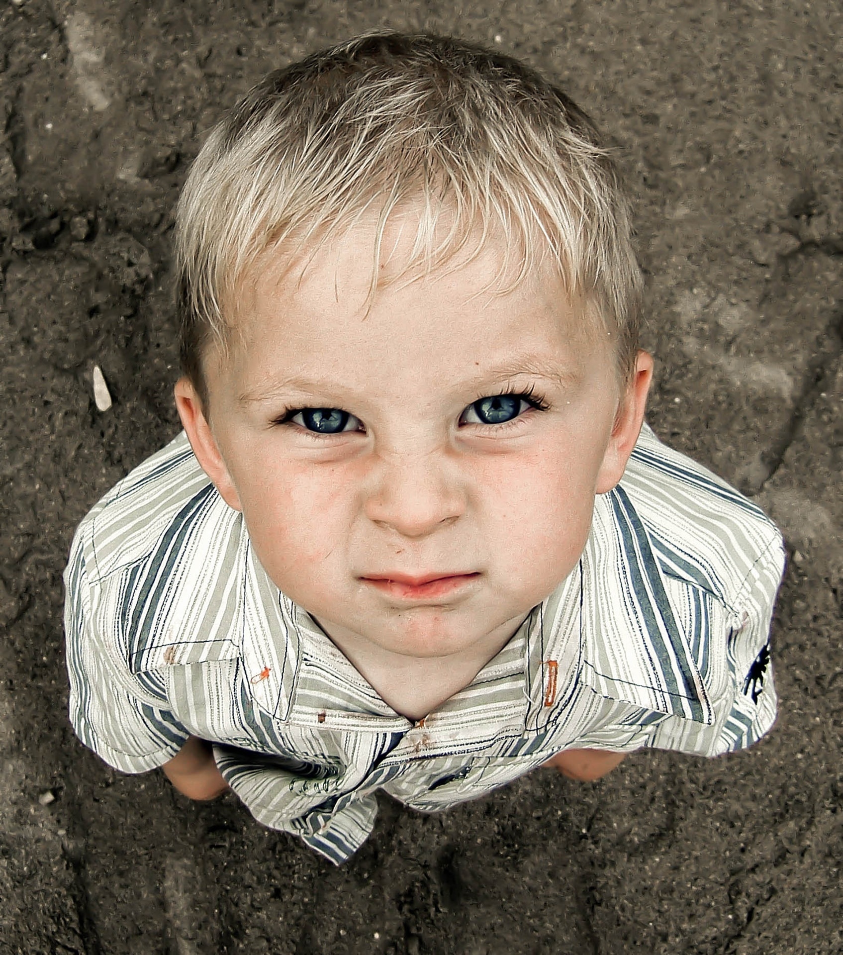boy in white, black, and grey stripe collared t-shirt standing in black sand