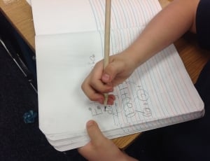 child writing mathematical equation on a lined paper on table thumbnail