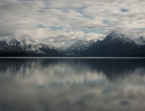 mirror image of snow covered mountains on body of water thumbnail