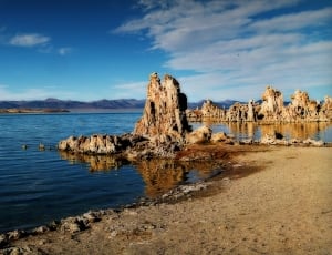 rock formation by body of water under blue cloudy skies thumbnail
