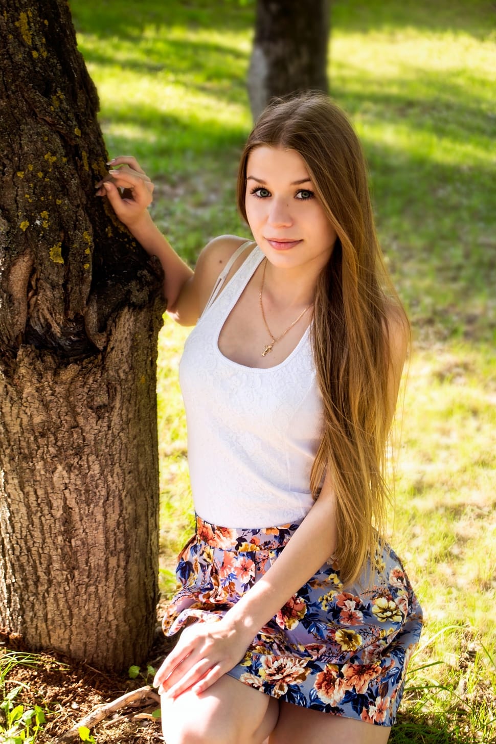photo of woman in white tank top and blue floral skirt near tree and grasses preview