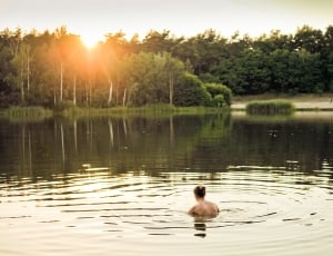 photography of person in the middle of body of water at sunset thumbnail