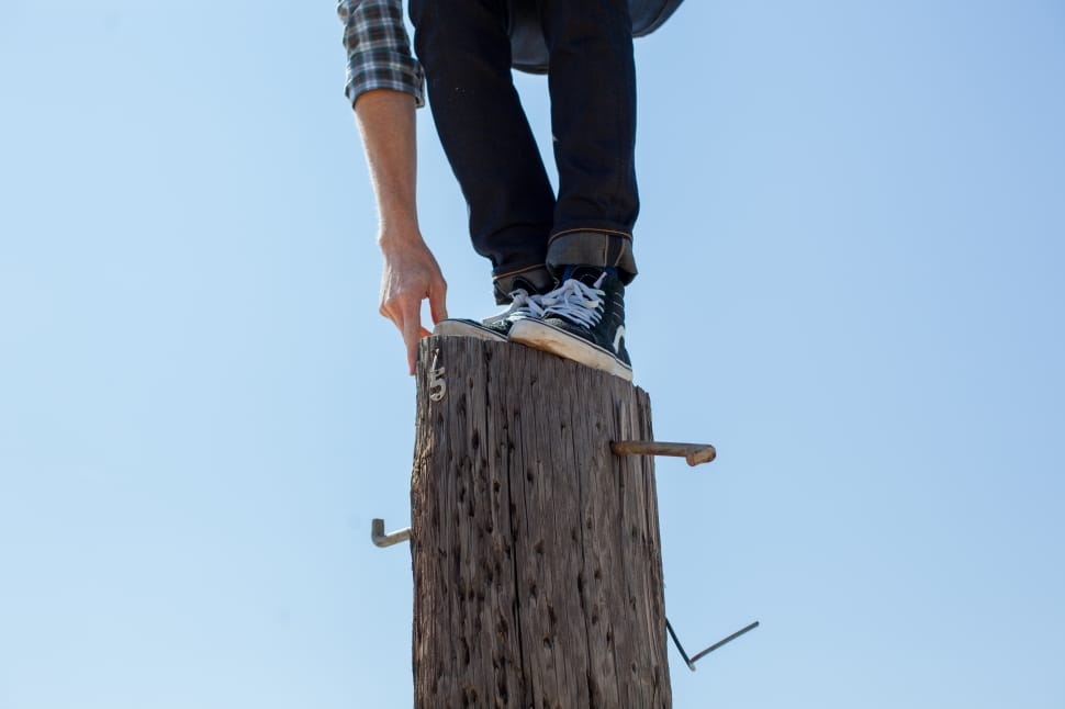 man wearing black jeans and black and white shirt standing on a tree trunk preview