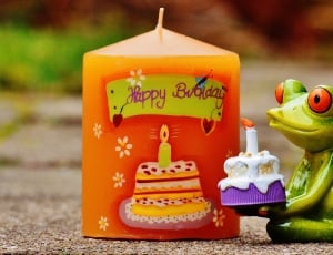 green frog holding cake beside orange happy birthday candle thumbnail