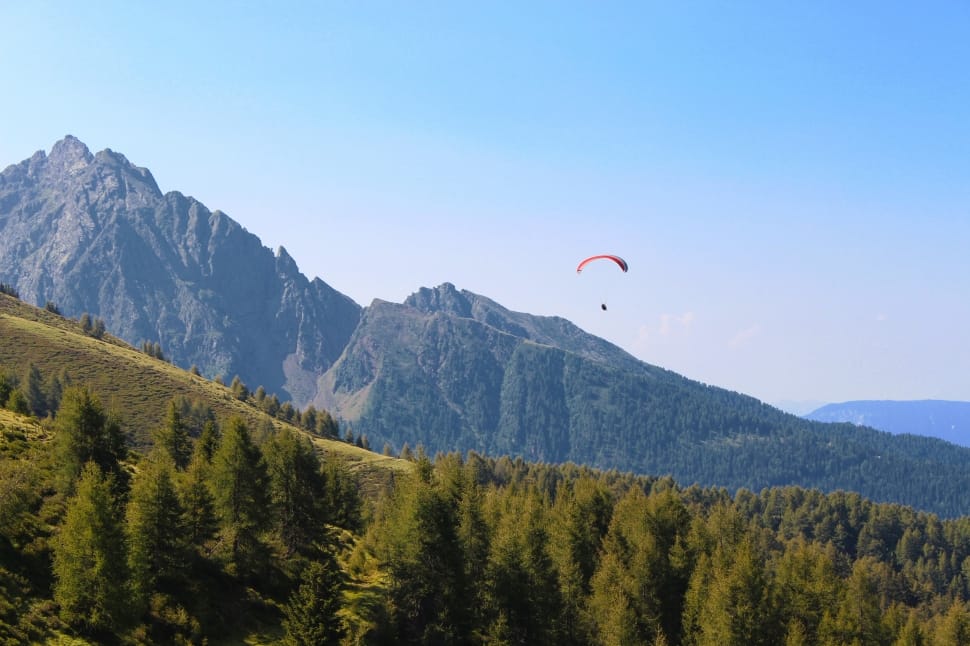 man doing skydiving under green tree mountains preview
