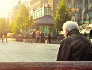 man in black leather jacket sitting on bench during daytime thumbnail