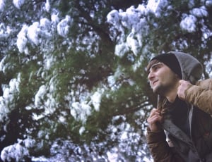 man wearing gray and brown snow jacket under and green leaves tree thumbnail