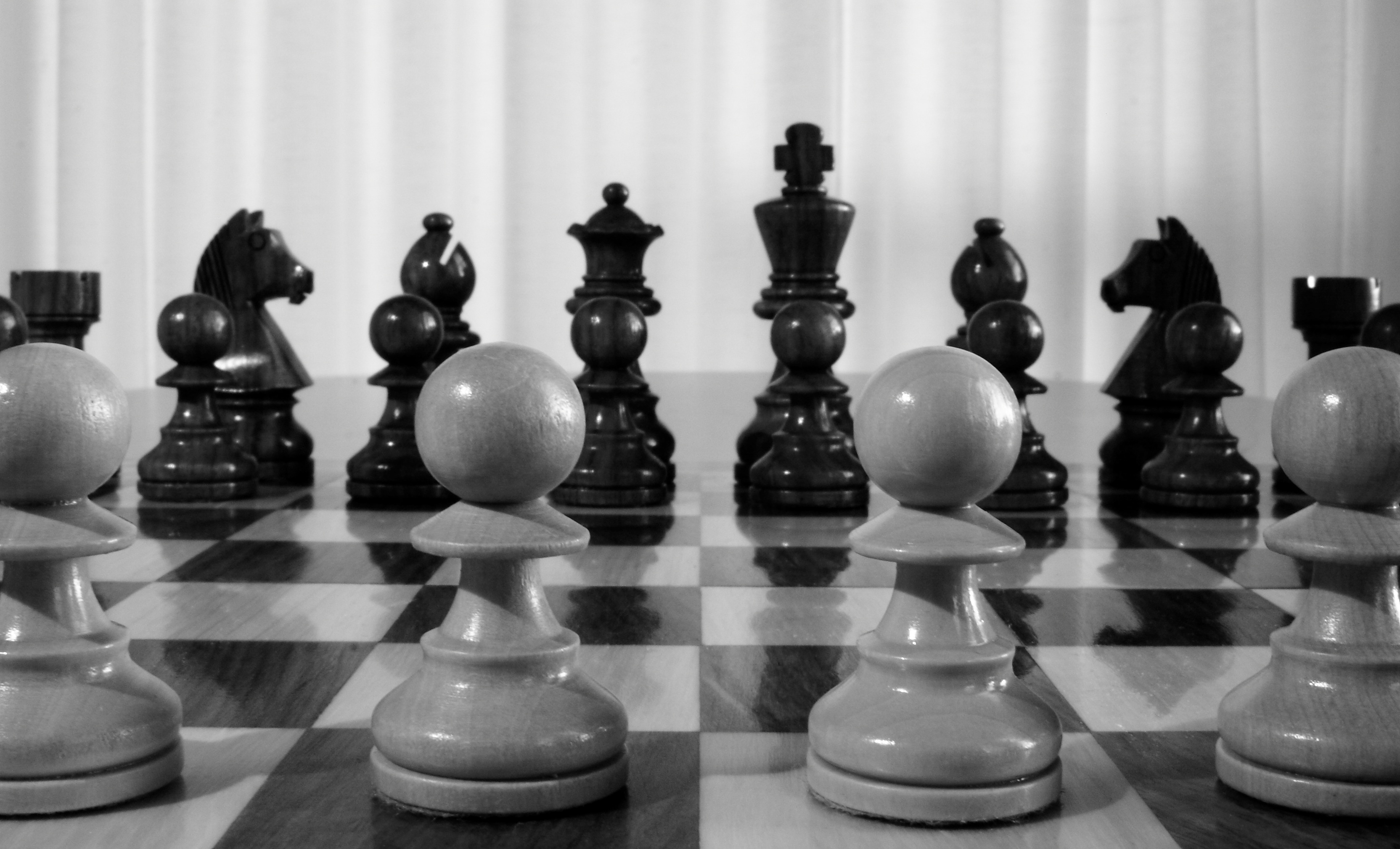 grayscale photo of white chess pawns in front of black chess pieces on chessboard