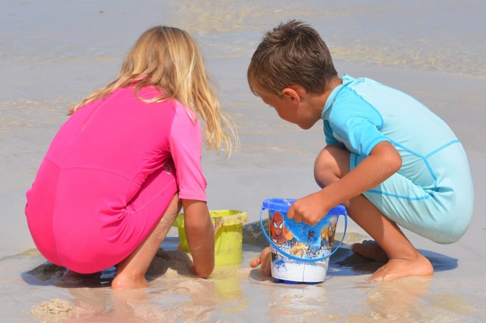 two child playing sand holding plastic buckets during daytime preview